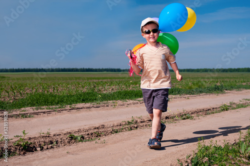 Little boy with colorful balloons walking the country road