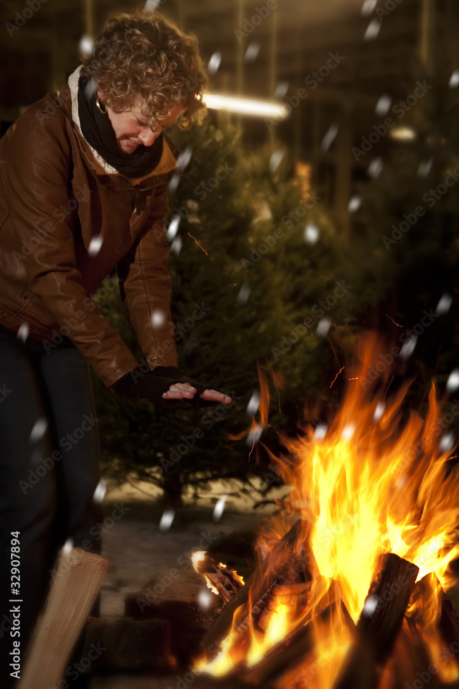 Woman warming hands by fire at christmas tree lot