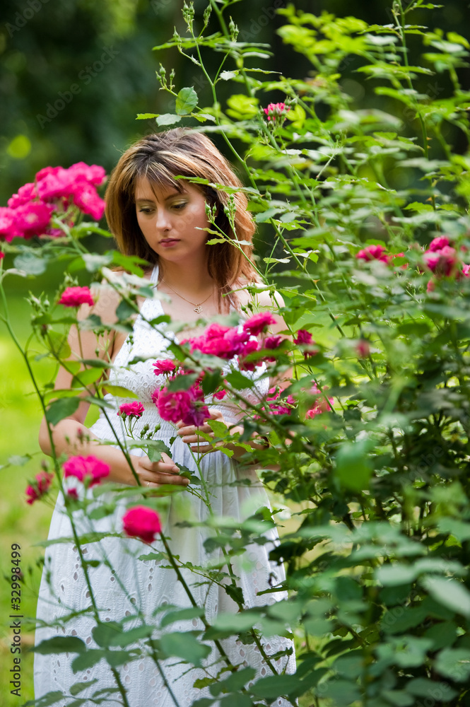 The girl stand against green leaves also smells flowers The girl stand against green leaves also smells flowers