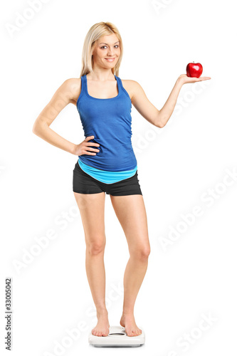 Smiling woman holding a red apple and standing on a weight scale