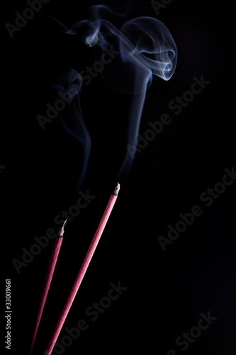 Smoke coming up from an incense stick over a black background © EwaStudio