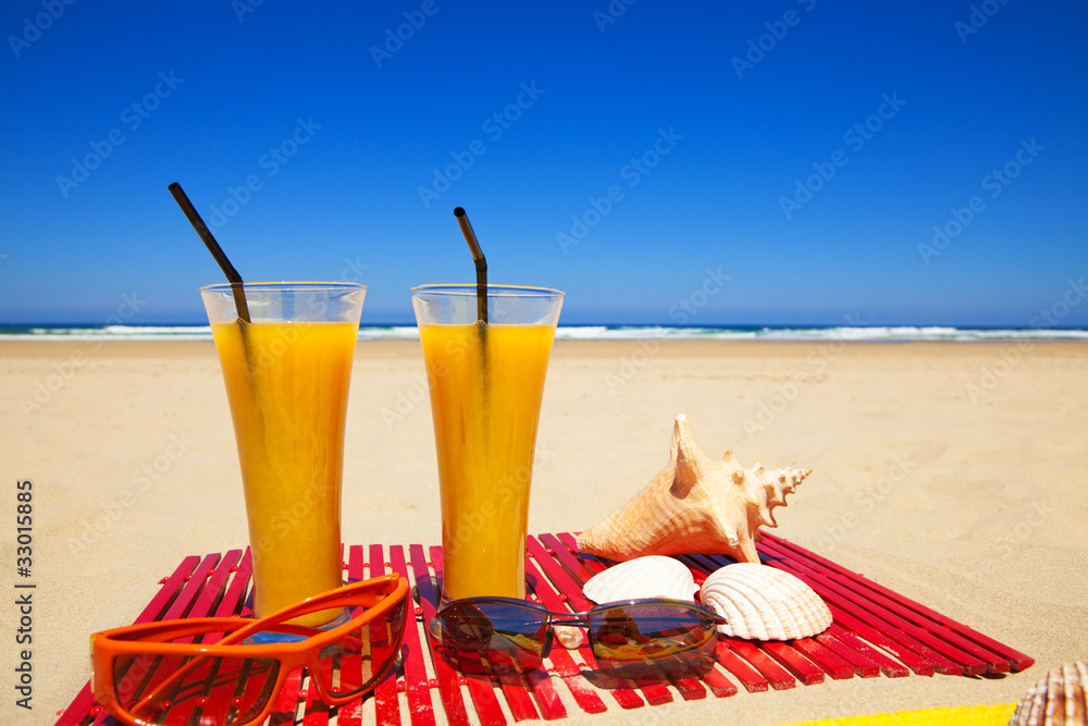 Orange juices, seashells and sunglasses on a deserted beach