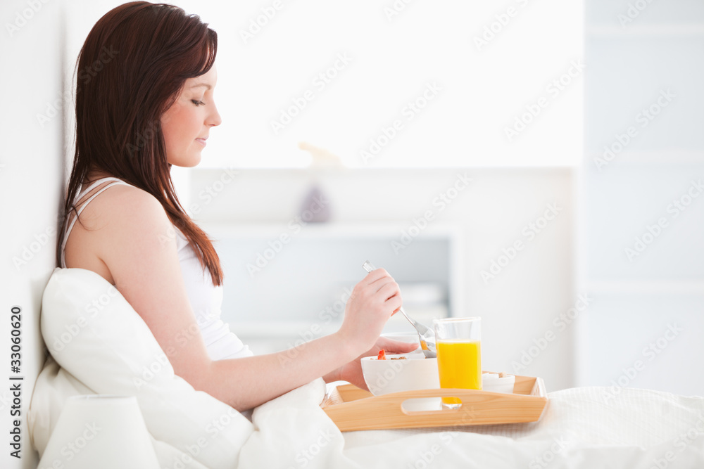 Cute red-haired female drinking a glass of orange juice while si Cute red-haired female drinking a glass of orange juice while si