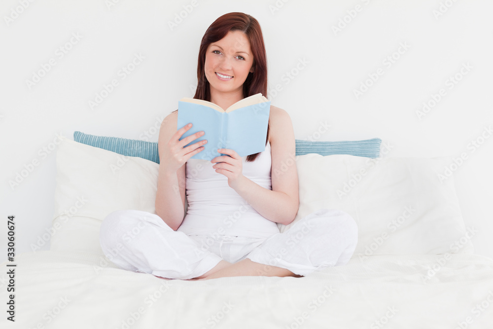 Gorgeous red-haired woman reading a book while sitting on her be Gorgeous red-haired woman reading a book while sitting on her be