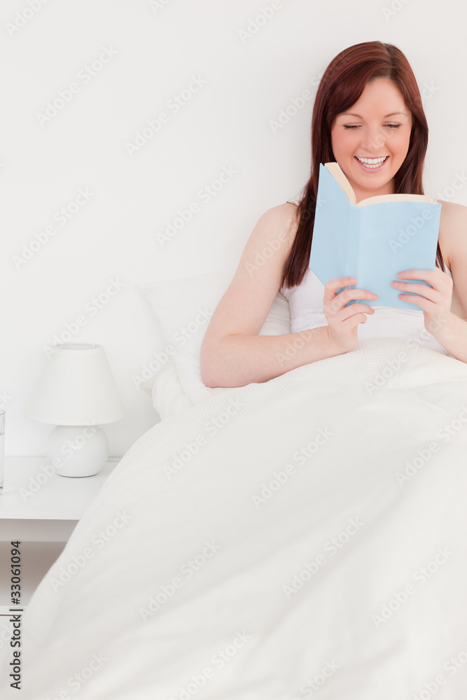 Pretty red-haired female reading a book while sitting on her bed Pretty red-haired female reading a book while sitting on her bed
