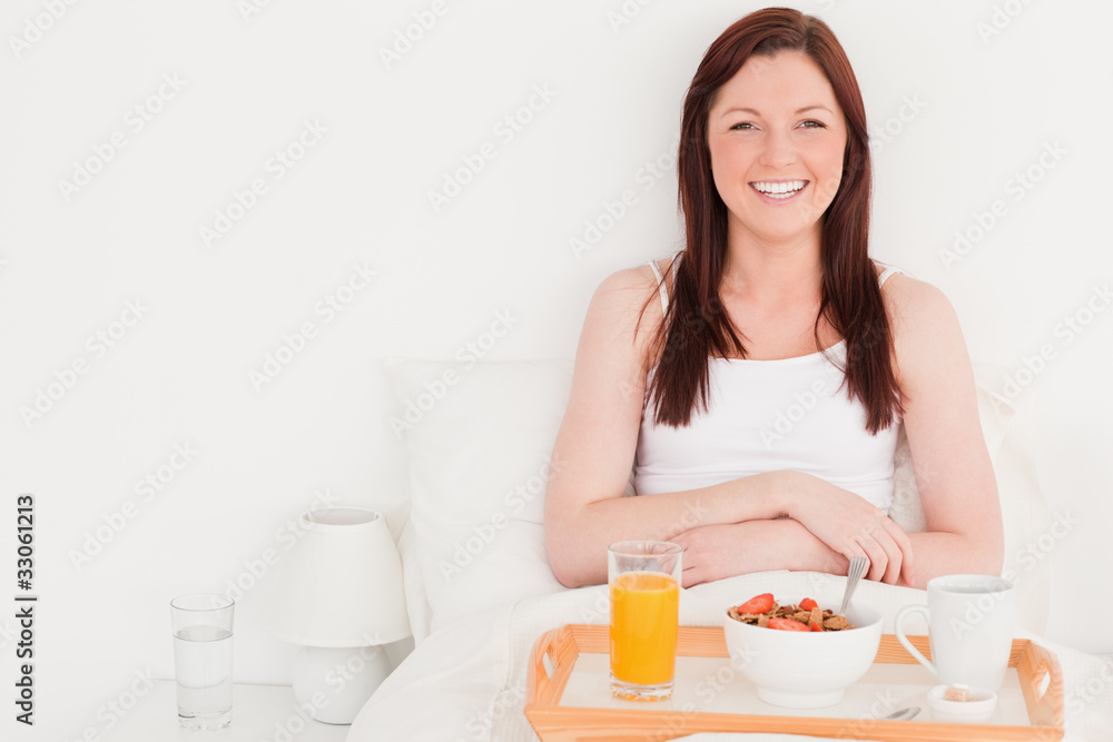 Beautiful red-haired woman having her breakfast while sitting on