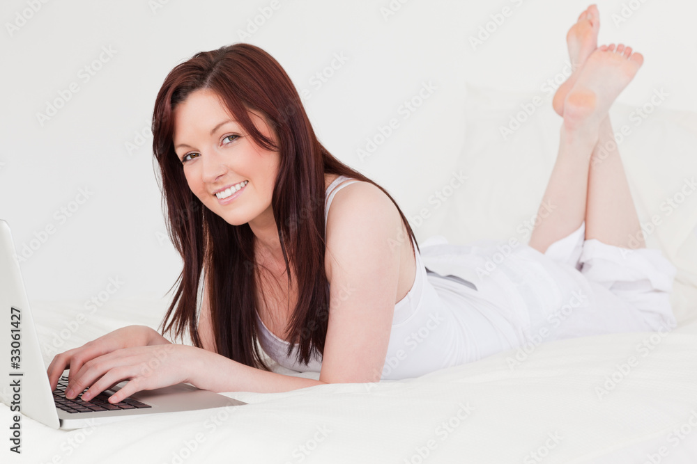 Pretty red-haired female relaxing with her laptop while lying on Pretty red-haired female relaxing with her laptop while lying on