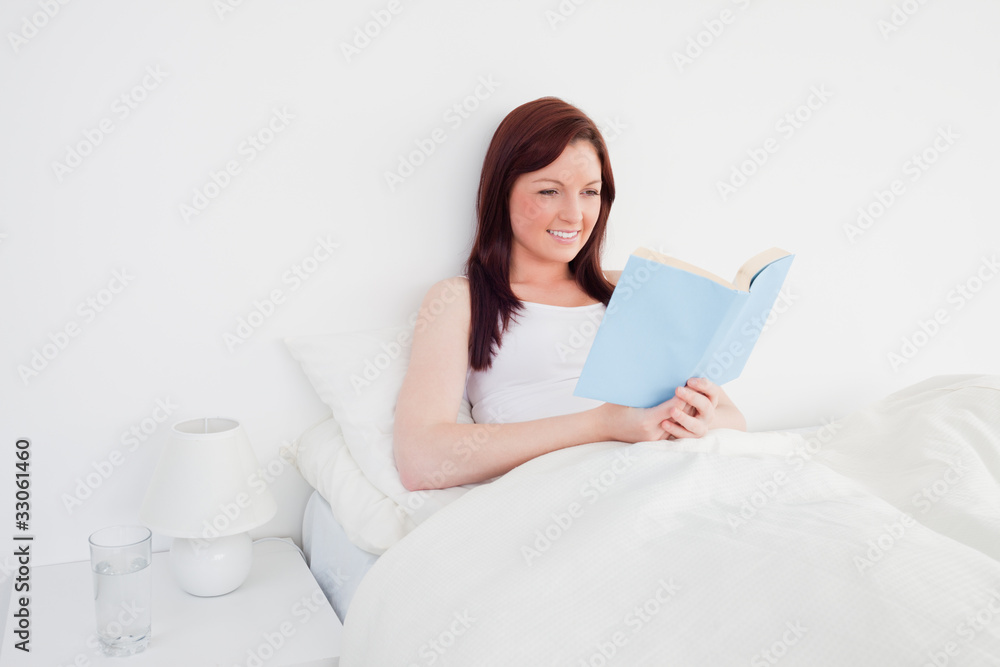 Beautiful red-haired woman reading a book while sitting on her b Beautiful red-haired woman reading a book while sitting on her b