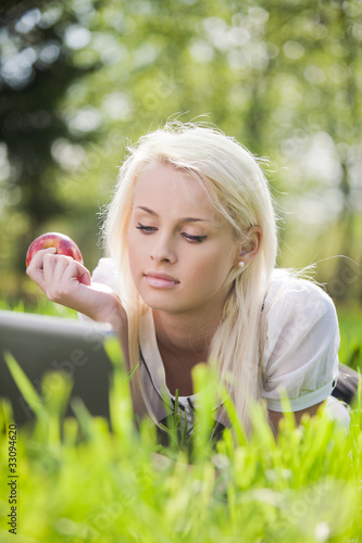 Young woman with laptop lying on the grass