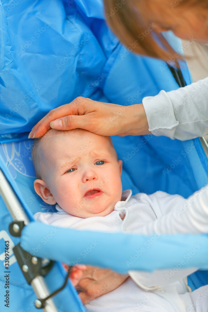 Caring mother soothing sitting in stroller crying baby girl. Caring mother soothing sitting in stroller crying baby girl.