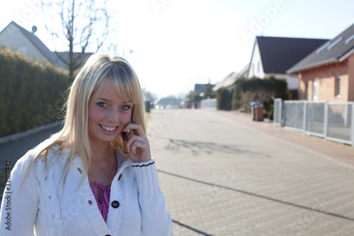 junge blonde frau telefoniert auf dorfstrasse photo