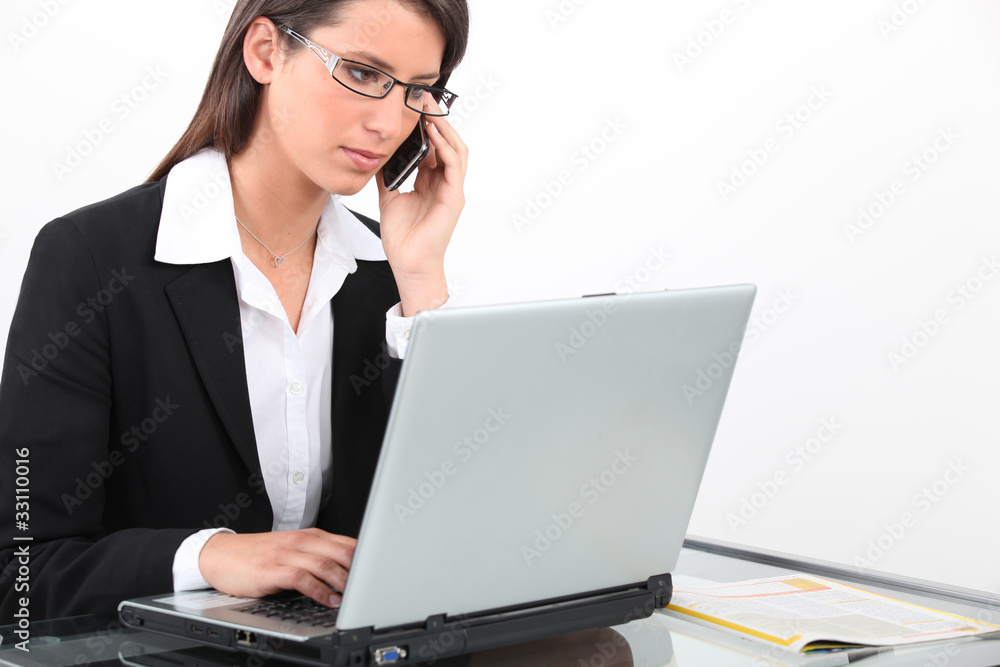 Brunette businesswoman using laptop and mobile telephone Brunette businesswoman using laptop and mobile telephone