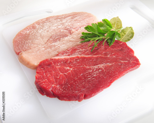 Raw pork chop and steak. Arrangement on white cutting board.