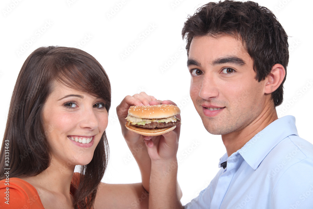 Studio shot of a young couple sharing a hamburger Studio shot of a young couple sharing a hamburger