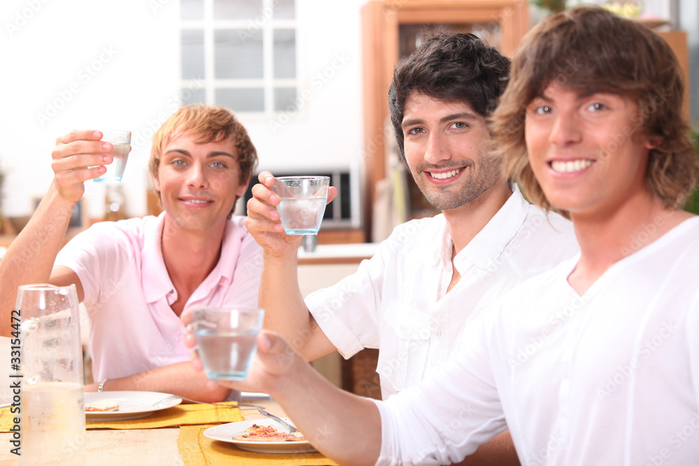 Three young men eating a meal together and drinking water Three young men eating a meal together and drinking water