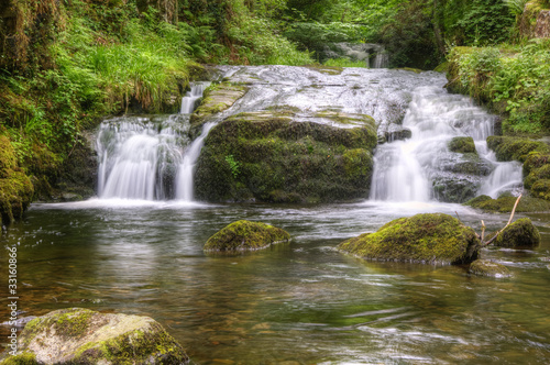 Stunning waterfall flowing over rocks through lush green forest © veneratio