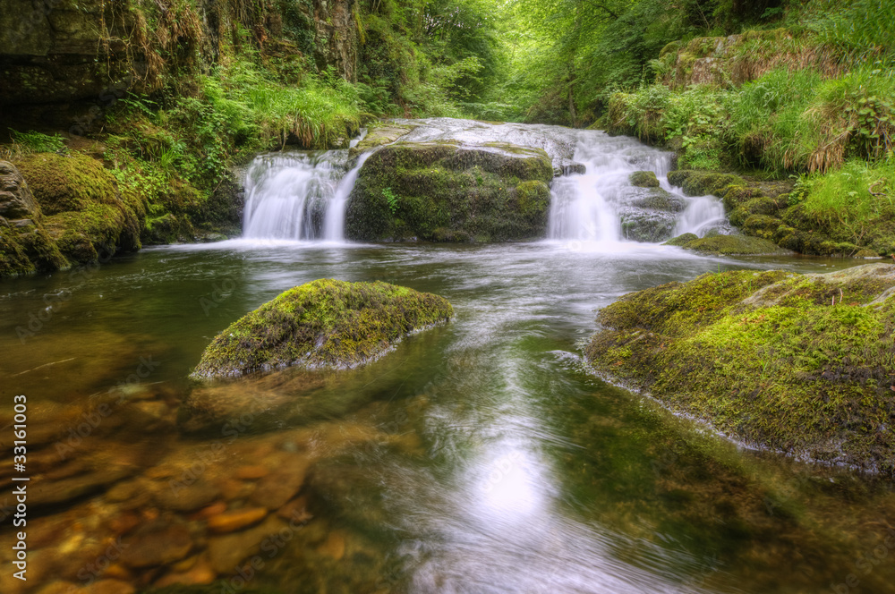Stunning waterfall flowing over rocks through lush green forest Stunning waterfall flowing over rocks through lush green forest
