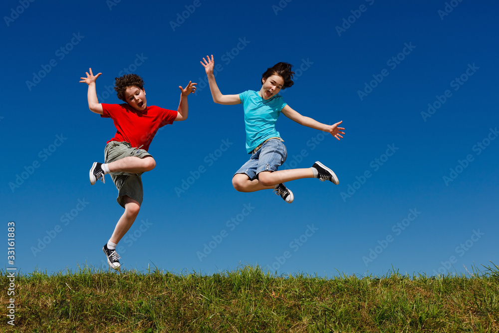 Girl and boy jumping, running against blue sky