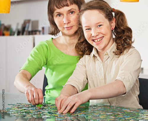 Teenager girl assembling jigsaw with her mother