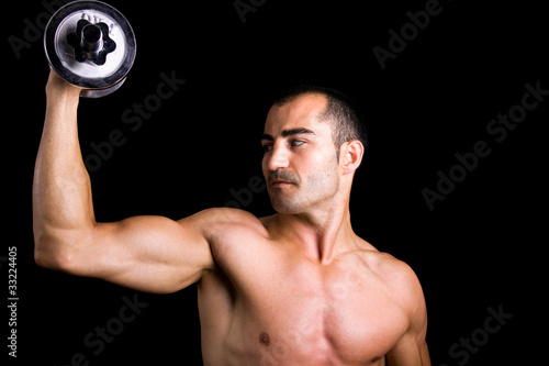 Muscular young man lifting dumbbells on black background.