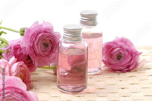 bottles with essential oil and pink dahlia flower on woven mat