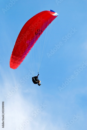 Red paraglider flying in blue sky