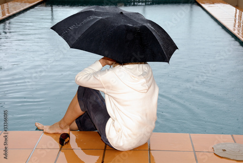 Frau sitzt am Schwimmbad im Regen