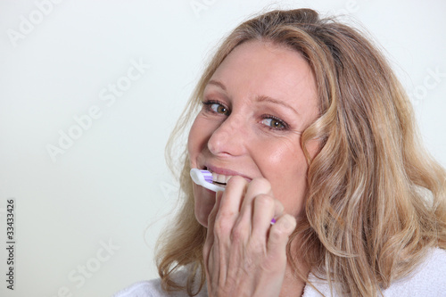 Blond woman smiling whilst brushing teeth