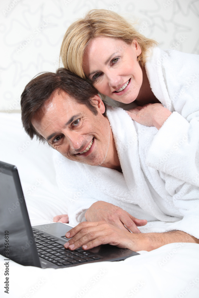 Happy couple on laptop in dressing gown.