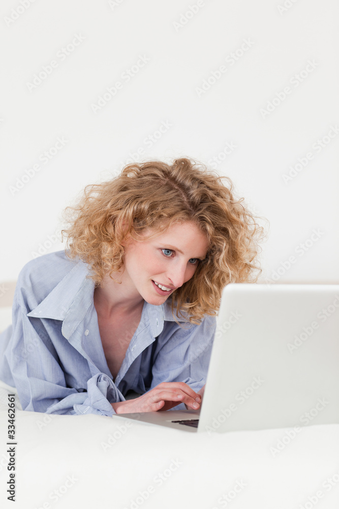 Pretty blonde female relaxing with her laptop while lying on her Pretty blonde female relaxing with her laptop while lying on her