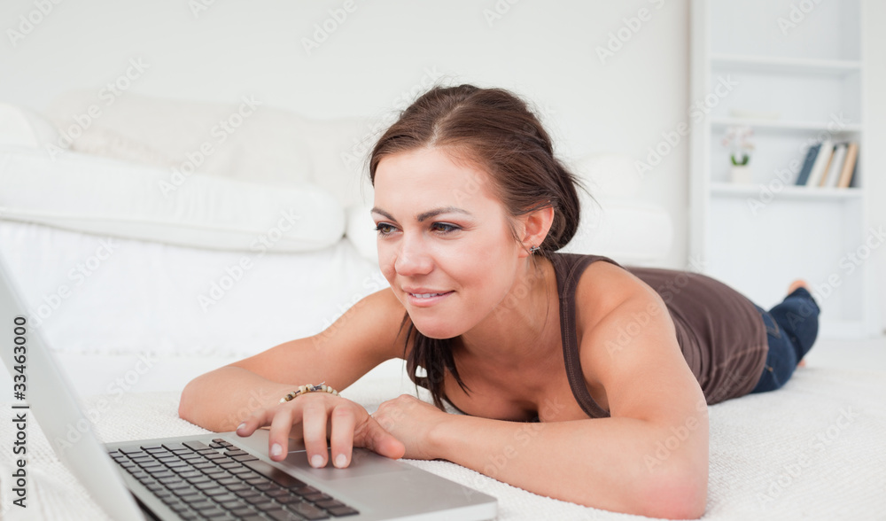 Young woman lying on a carpet with a laptop Young woman lying on a carpet with a laptop