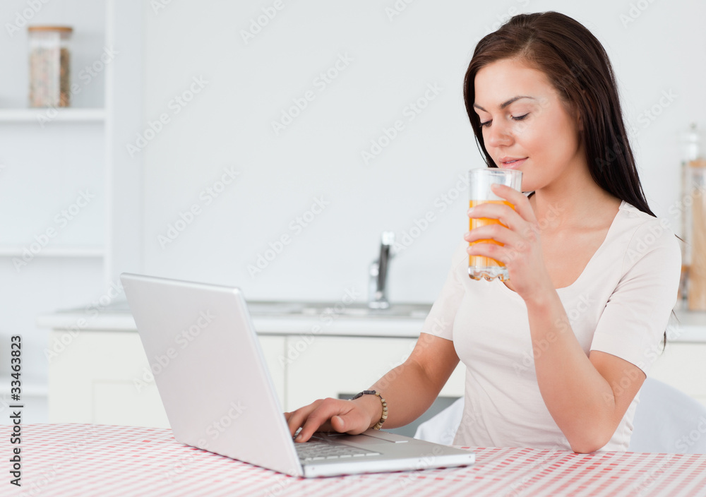 Brunette using her laptop and drinking orange juice Brunette using her laptop and drinking orange juice