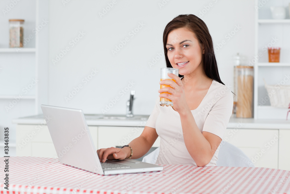 Young woman using her laptop and drinking orange juice Young woman using her laptop and drinking orange juice