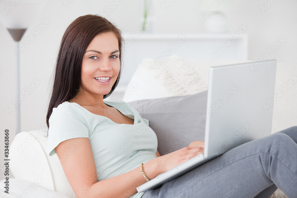 Beautiful woman typing on her laptop while sitting on her sofa Beautiful woman typing on her laptop while sitting on her sofa