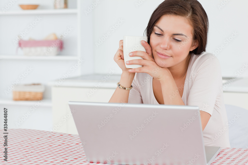 Cute dark-haired woman using her laptop and having a tea Cute dark-haired woman using her laptop and having a tea