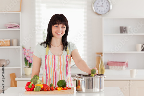 Attractive brunette woman posing while cooking vegetables