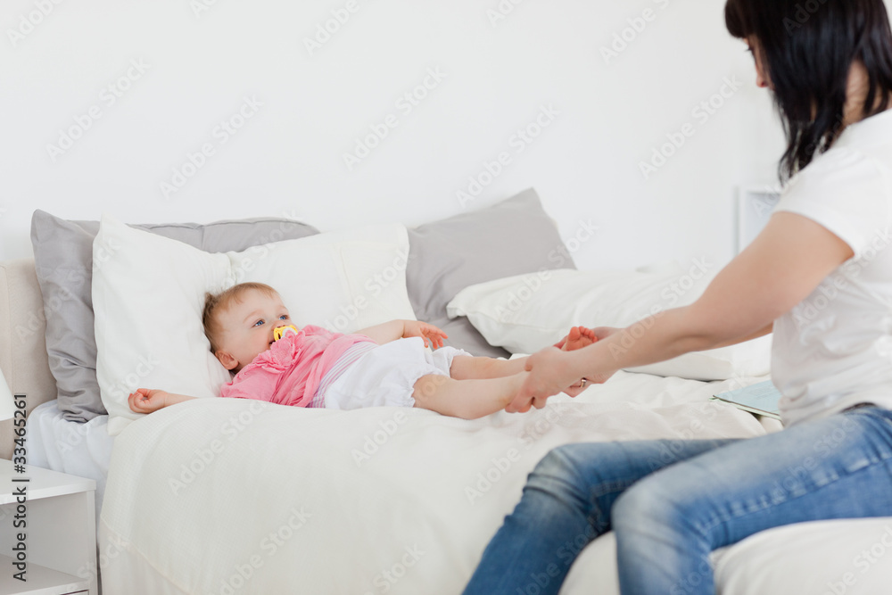 Cute brunette woman playing with her baby while sitting on a bed Cute brunette woman playing with her baby while sitting on a bed