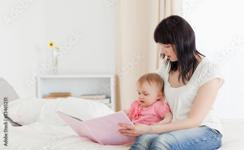 Attractive brunette woman showing a book to her baby while sitti