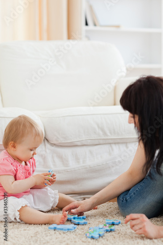 Attractive woman and her baby playing with puzzle pieces while s