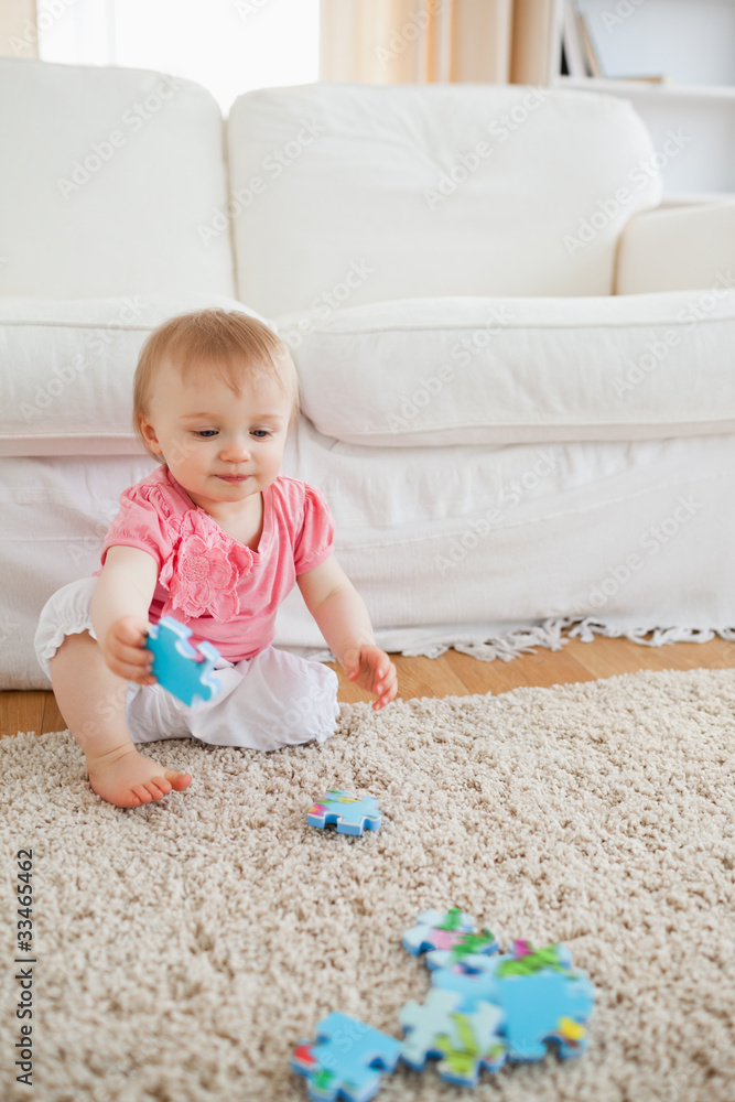 Lovely blond baby playing with puzzle pieces while sitting on a Lovely blond baby playing with puzzle pieces while sitting on a
