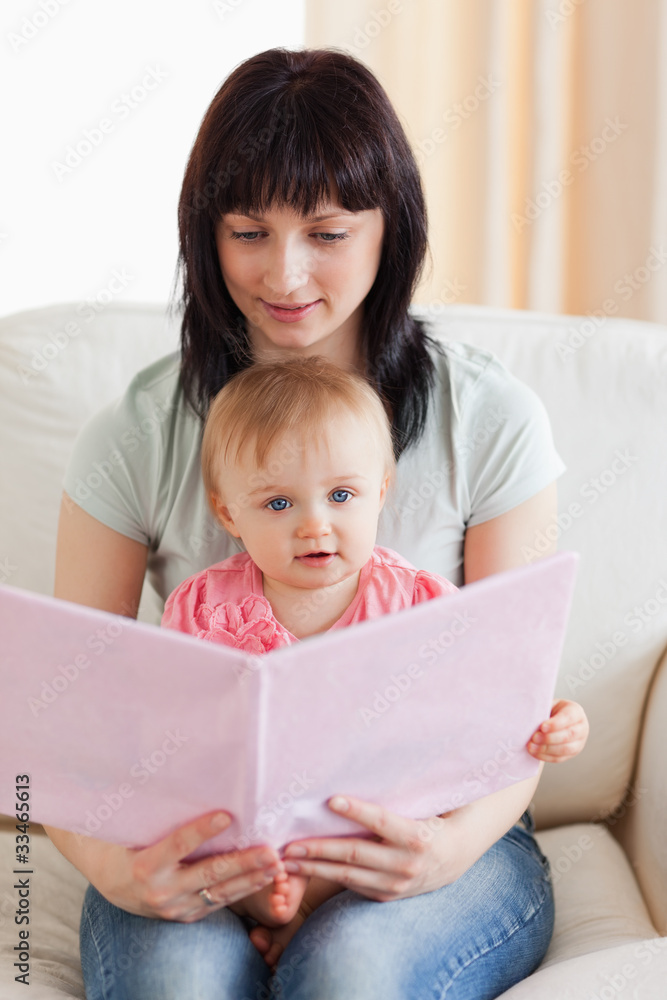 Attractive woman holding her baby and a book in her arms while s Attractive woman holding her baby and a book in her arms while s