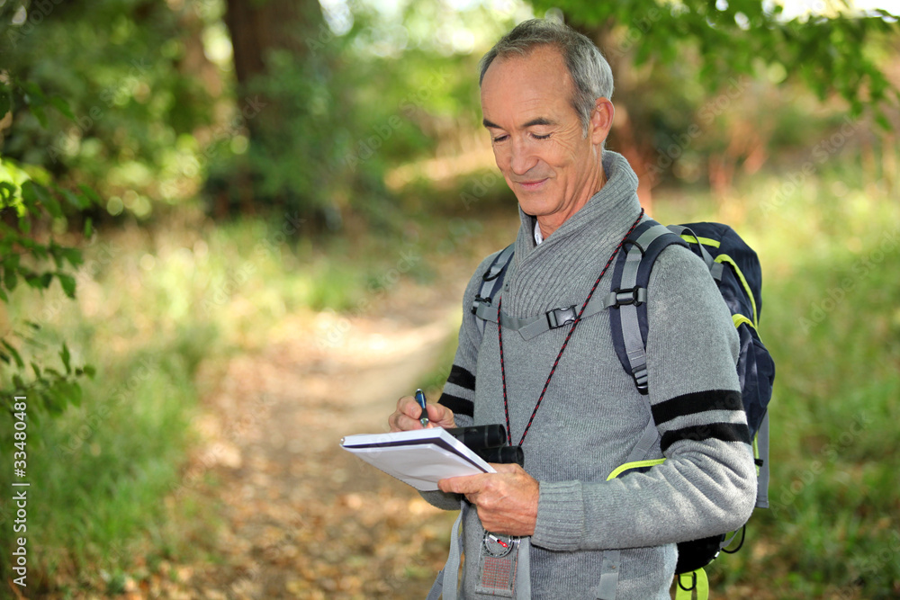 Fototapeta premium sixty years old man taking notes on a forest trail