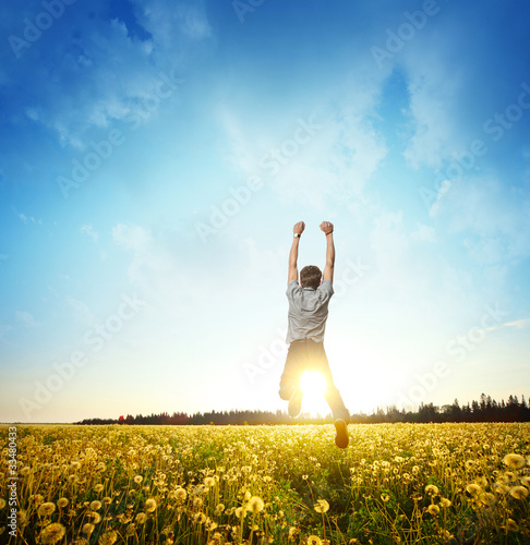 Fototapeta Naklejka Na Ścianę i Meble -  Young man jumping on meadow with dandelions on cloudy background