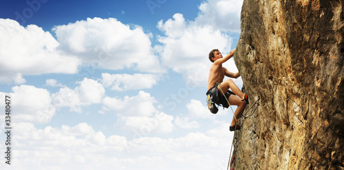 A young man climbs on a cliff over blue sky background