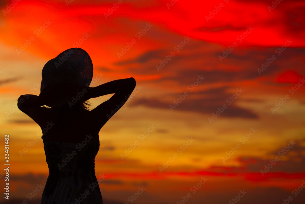 Silhouette of woman in hat on orange sunset background