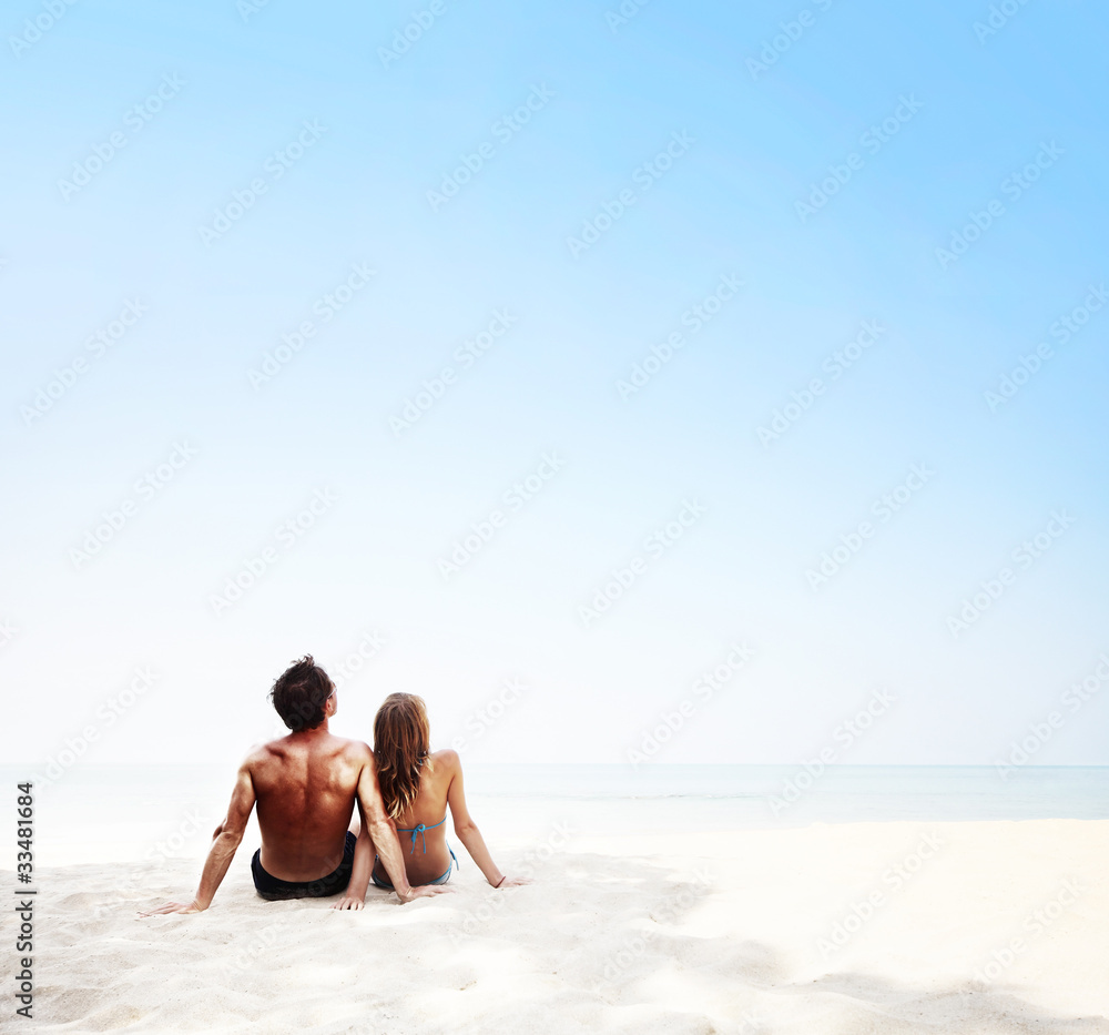 Young couple sitting on white sand by sea and enjoying each other