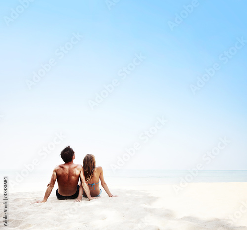 Young couple sitting on white sand by sea and enjoying each other