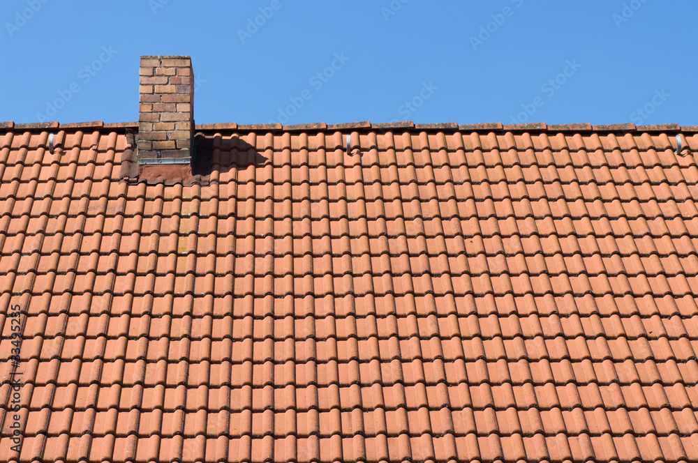 The roof of tiles and chimney against a blue sky.