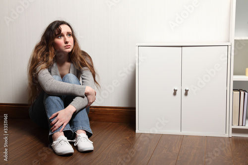 Anxious teenage girl sits alone on floor at home