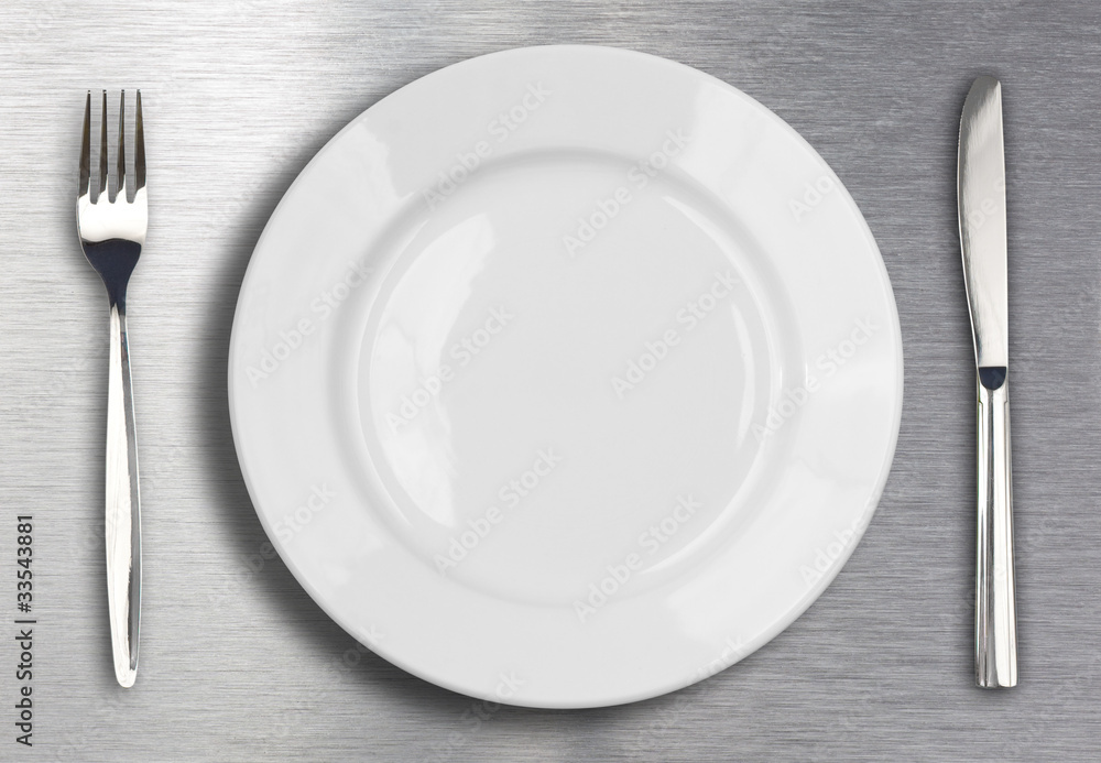 Knife, white plate and fork on metal background